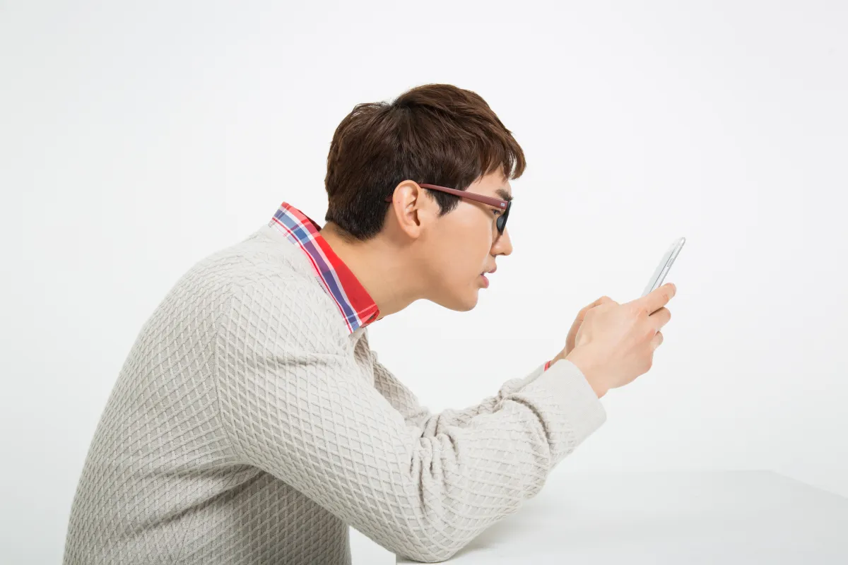 안경을 쓴 젊은 남성이 스마트폰 화면을 가까이 들여다보는 모습