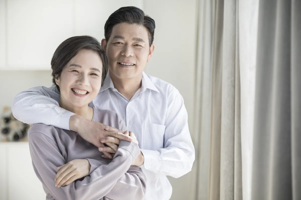 집 안에서 서로 안고 환하게 웃는 한국인 중년 부부