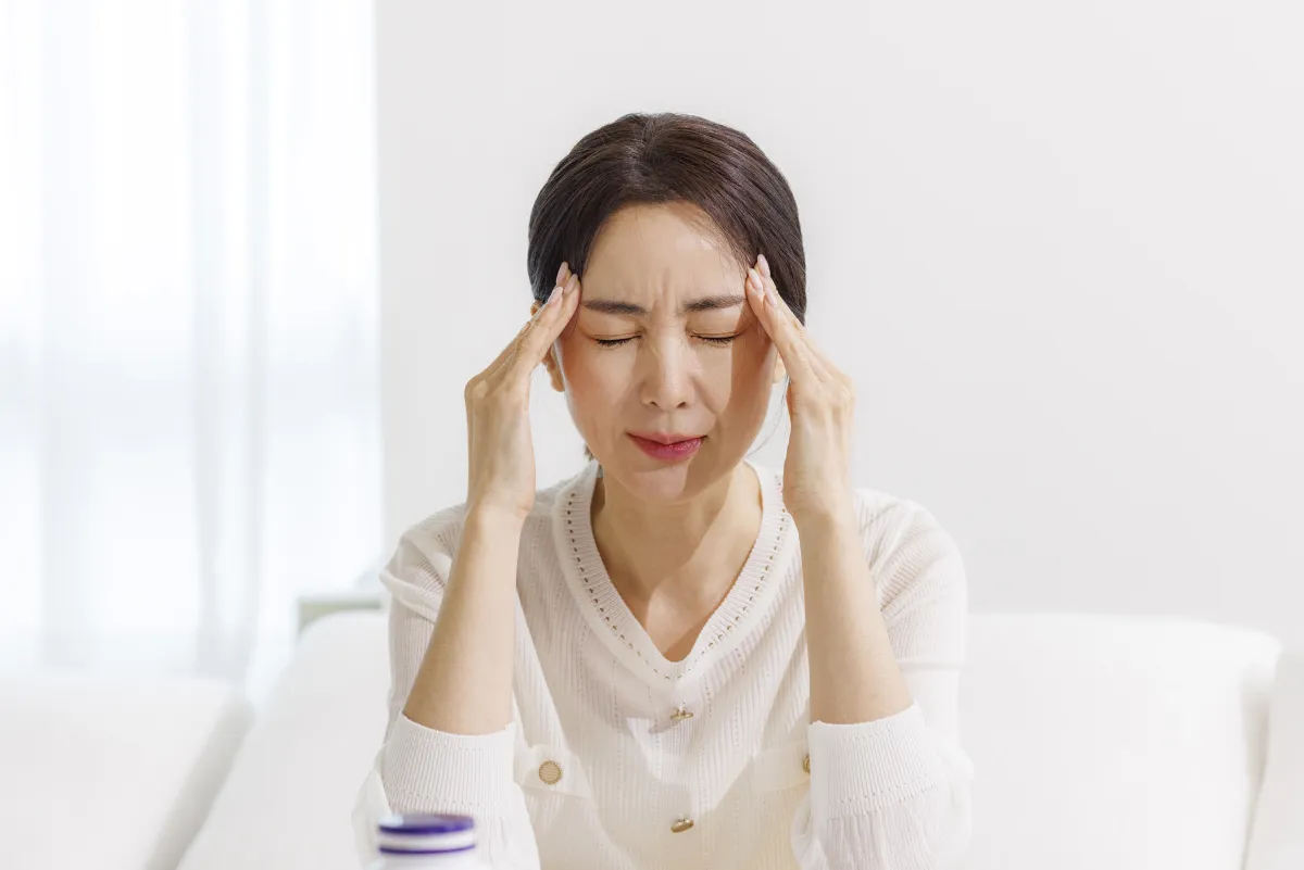 한쪽 관자놀이와 얼굴 옆을 양손으로 짚고 눈을 찡그린 중년 여성