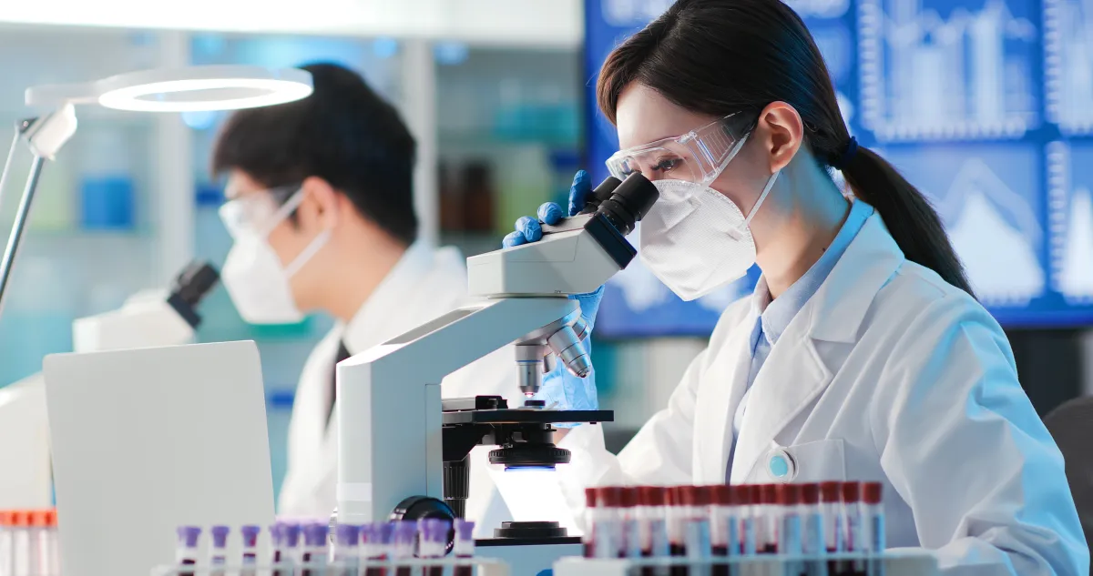 검사실에서 혈액 검체 튜브를 옆에 두고 현미경을 들여다보는 연구원들