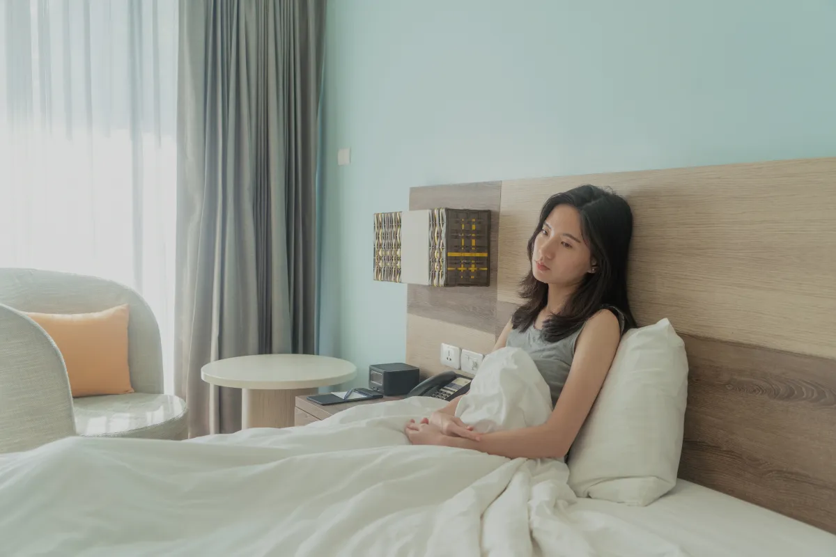 낮인데도 침대에서 일어나지 못하고 이불을 덮은 채 벽에 기대앉아 있는 여성